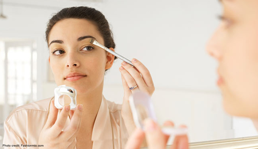 A woman applies eye shadow as she looks at her reflection in the mirror. 